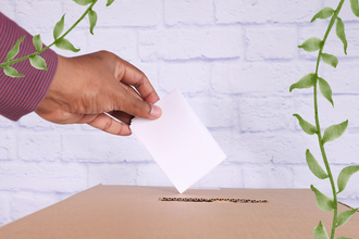 A hand placing a voting slip in a ballot box