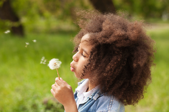 A young girl holding a dandelion and blowing seeds