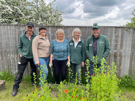 Group of volunteers standing in front of a fence with a selection of wild flowers in front of them