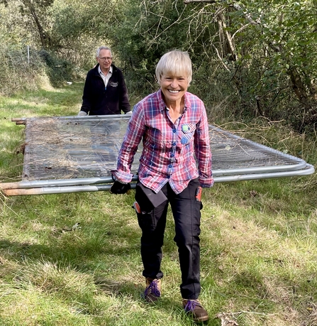 Two volunteers carrying fencing panels along a grassy track