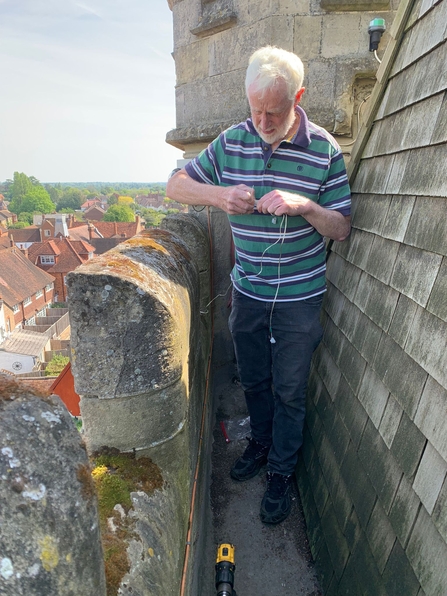 Man standing at the top of a church tower holding small electrical equipment