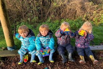 Four toddlers sitting on a bench using binoculars