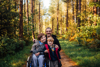 Two boys, one a wheelchair user, and their dad on a woodland path