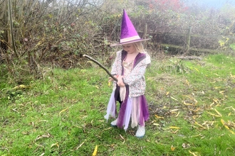 girl in a purple witch costume standing on grass