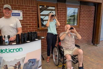 an Opticron stand and two people testing out binoculars
