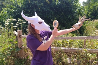 person with an animal skull on their head looking at another skull through a magnifying glass