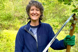 Philippa smiling at the camera with a scythe in hand.