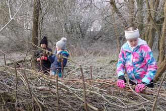 three young people building a fence out of dead branches in a forest on a cloudy day