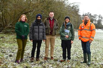 A group of five people stood in a field, with a dusting of snow on the ground and bare trees in the background. They are smiling at the camera.