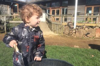 Close-up image of a young child with a trowel in their hand, with Sutton Courtenay Environmental Education Centre in the background