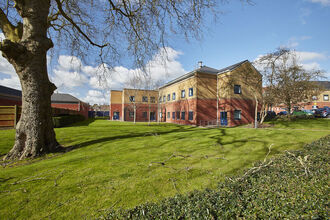 A large two storey building next to a large area of grass with some trees