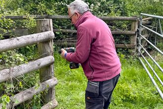 A volunteer holding a drill against a fence post