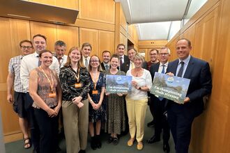 A group of people dressed smartly in a hallway, smiling at the camera. Two are holding signs which read: I am championing chalk streams