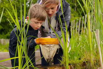 boy and woman look into pond net whilst standing over pond