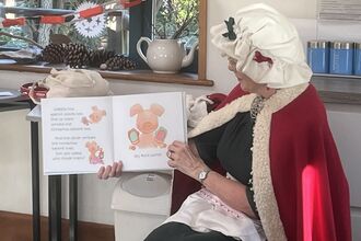 Image of Mrs Claus in her festive bonnet and cape reading a story.