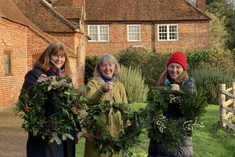 Image of three women in the Woolley Firs Environmental Education Centre garden holding their hand-crafted festive wreaths