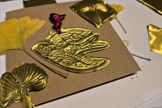 Image of the results of a metal embossing workshop. An intricate design of a bird is inlaid into a gold plate.