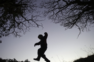 Young boy silhouetted at dusk playing on edge of woodland