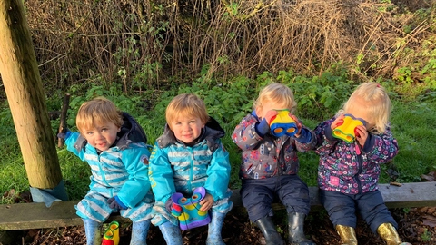 Four toddlers sitting on a bench using binoculars