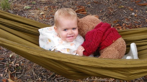 A child sits in  hammock with their teddy bear