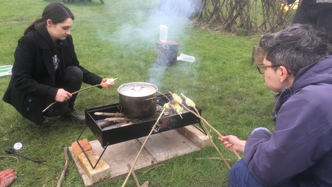 Two adults cook rounda  campfire