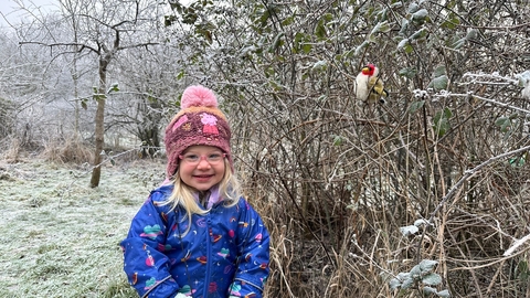 A smiling child next to a frosty hedge