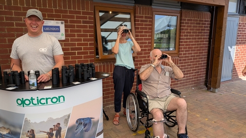 an Opticron stand and two people testing out binoculars