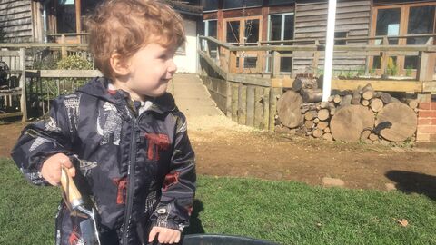 Close-up image of a young child with a trowel in their hand, with Sutton Courtenay Environmental Education Centre in the background
