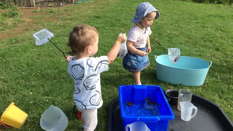 Image of two young children playing with pond-dipping equipment. They have nets in their hands and are looking at pond creatures in containers