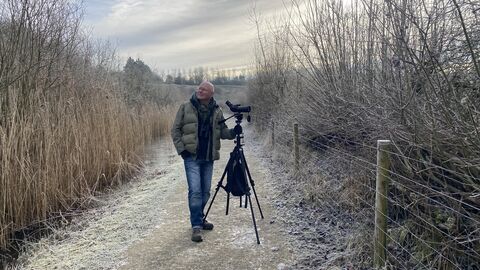 Man stands with scope and tripod on college lake reedbed path