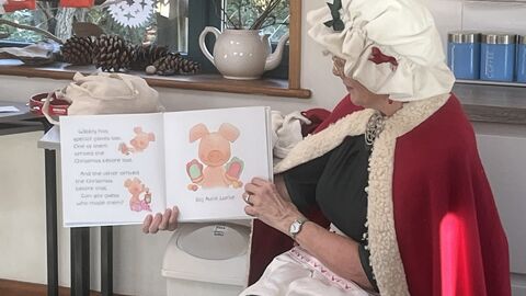 Image of Mrs Claus in her festive bonnet and cape reading a story.