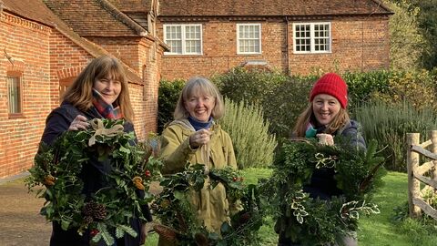 Image of three women in the Woolley Firs Environmental Education Centre garden holding their hand-crafted festive wreaths