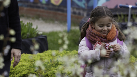 A small girl is looking at colourful flowers in her hands and smiling