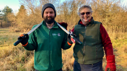 Two people smiling at the camera in a woodland clearing