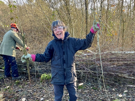 Woman smiling at the camera in front of a dead hedge