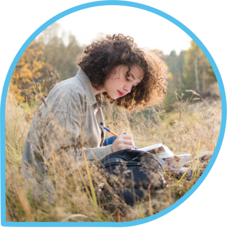 Teenage girl sat in a field with a book, studying outdoors