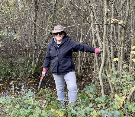 Person holding a small saw standing next to thin tree trunks