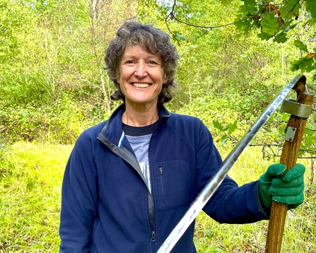 Philippa smiling at the camera with a scythe in hand.