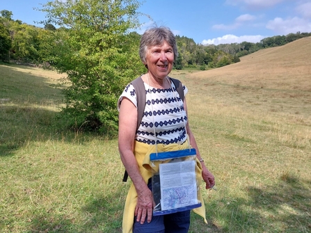 A lady walking through a grassy valley with trees in the distance