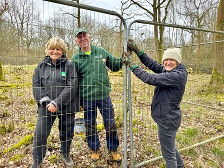 Three people stood beside a metal fence.