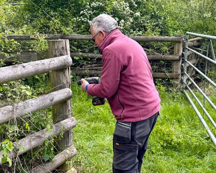 A volunteer holding a drill against a fence post