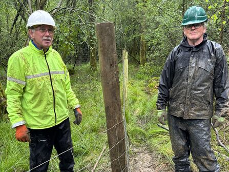 Two people in helmets and jackets stood on either side of a fence post