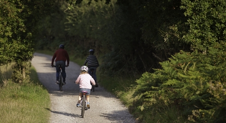 Family cycling along wooded path. 