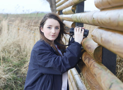 Young woman holding binoculars at a wetland nature reserve