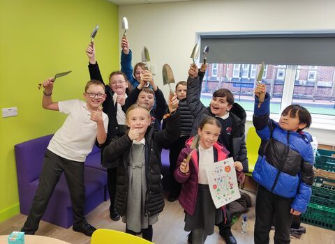 School kids holding garden tools in the air. 