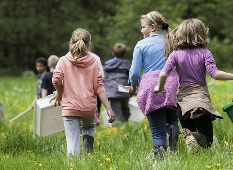 Schoolchildren walking through a field with buckets and trays to release salmon fry in a river